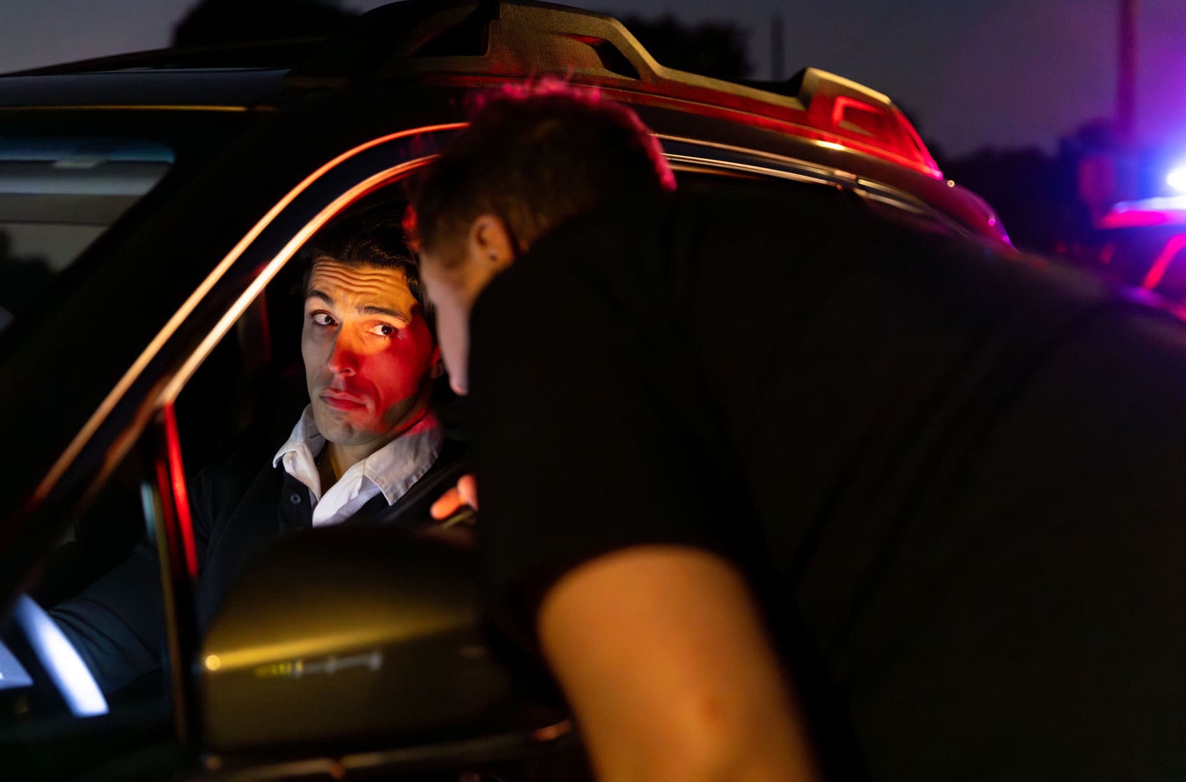 person-slumped-over-the-wheel-of-a-car-with-emergency-lights-behind-them